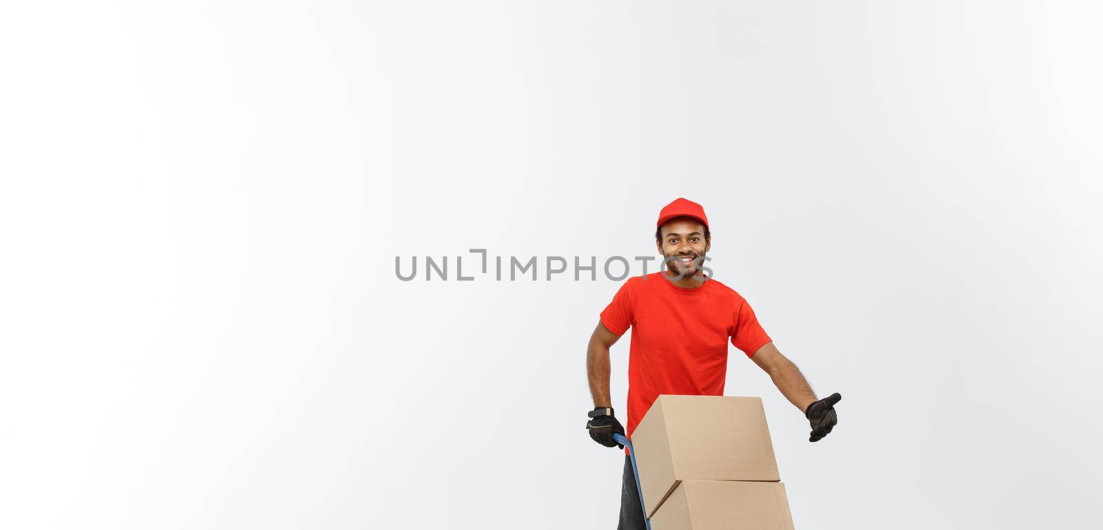 Delivery Concept - Portrait of Handsome African American delivery man or courier pushing hand truck with stack of boxes. Isolated on Grey studio Background. Copy Space