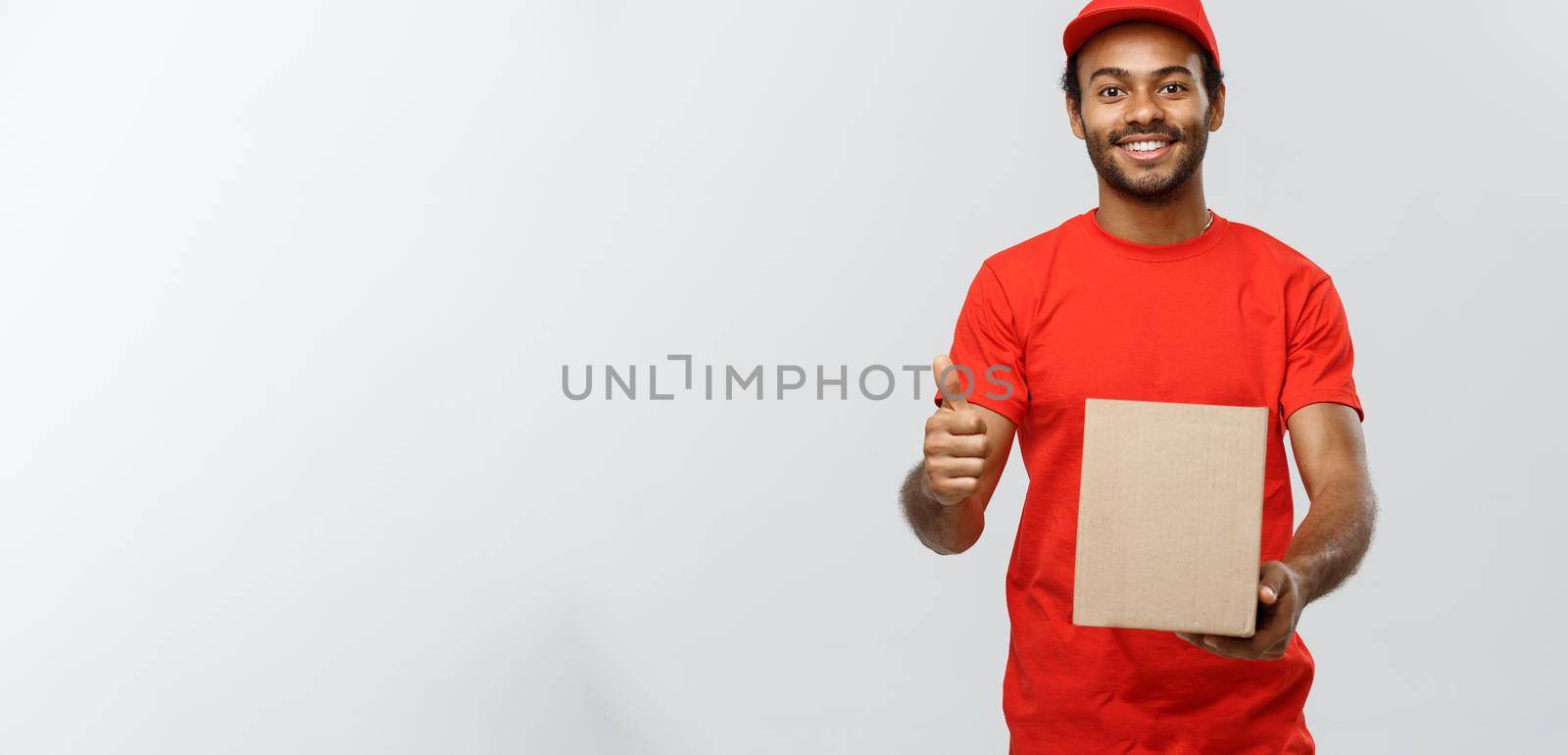 Delivery Concept - Portrait of Happy African American delivery man holding a box package and showing thumps up. Isolated on Grey studio Background. Copy Space