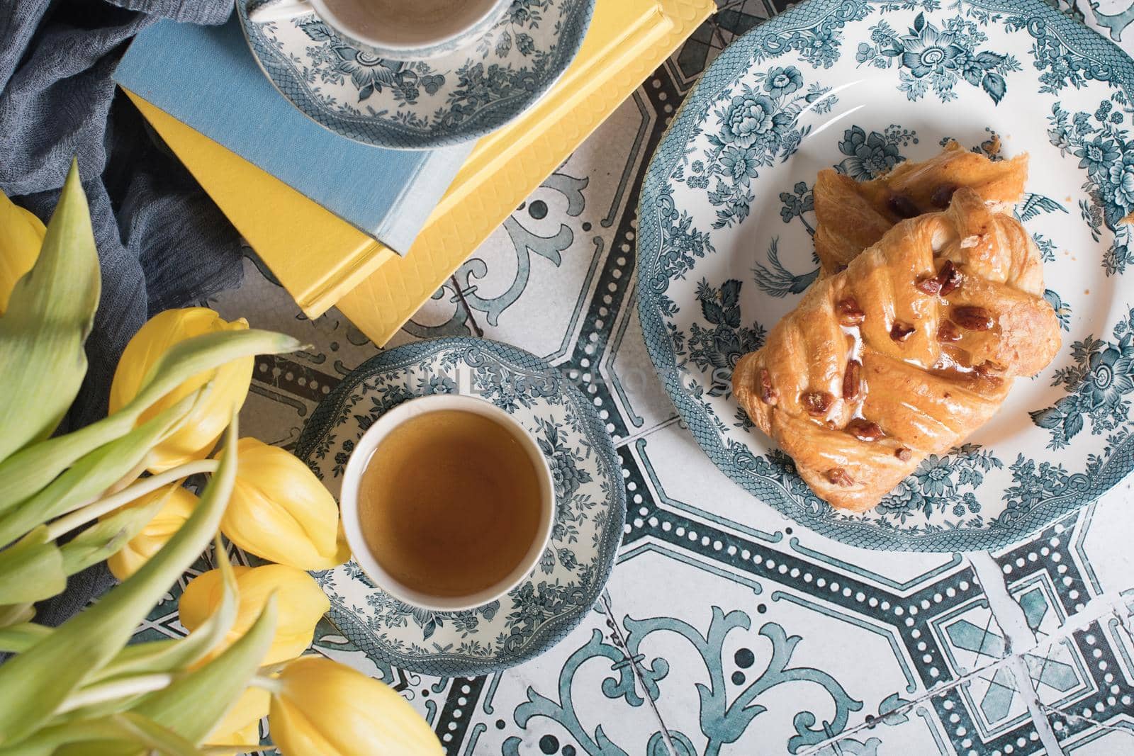 flat lay food, sweet puff, tea in a vintage porcelain cup and a stack of books, a bouquet of yellow withering tulips in a vase,. High quality photo