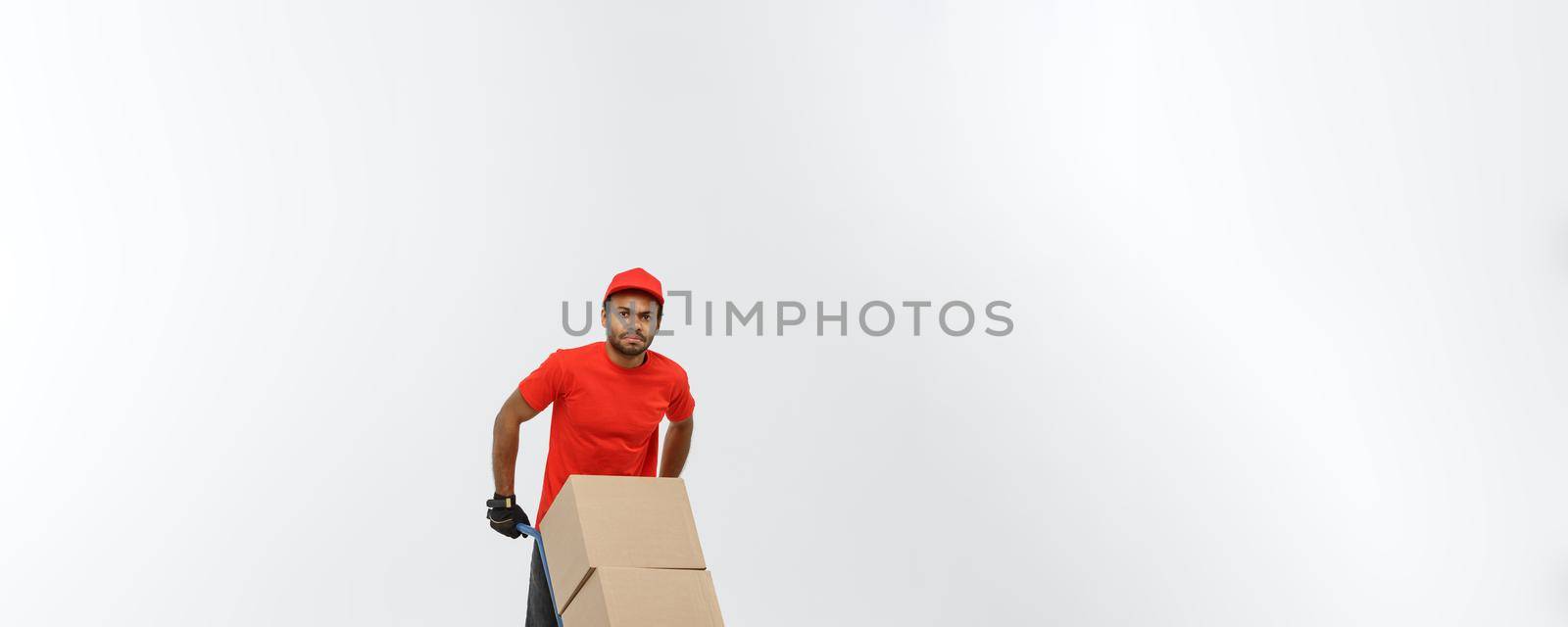 Delivery Concept - Portrait of Handsome African American delivery man or courier pushing hand truck with stack of boxes. Isolated on Grey studio Background. Copy Space. by Benzoix
