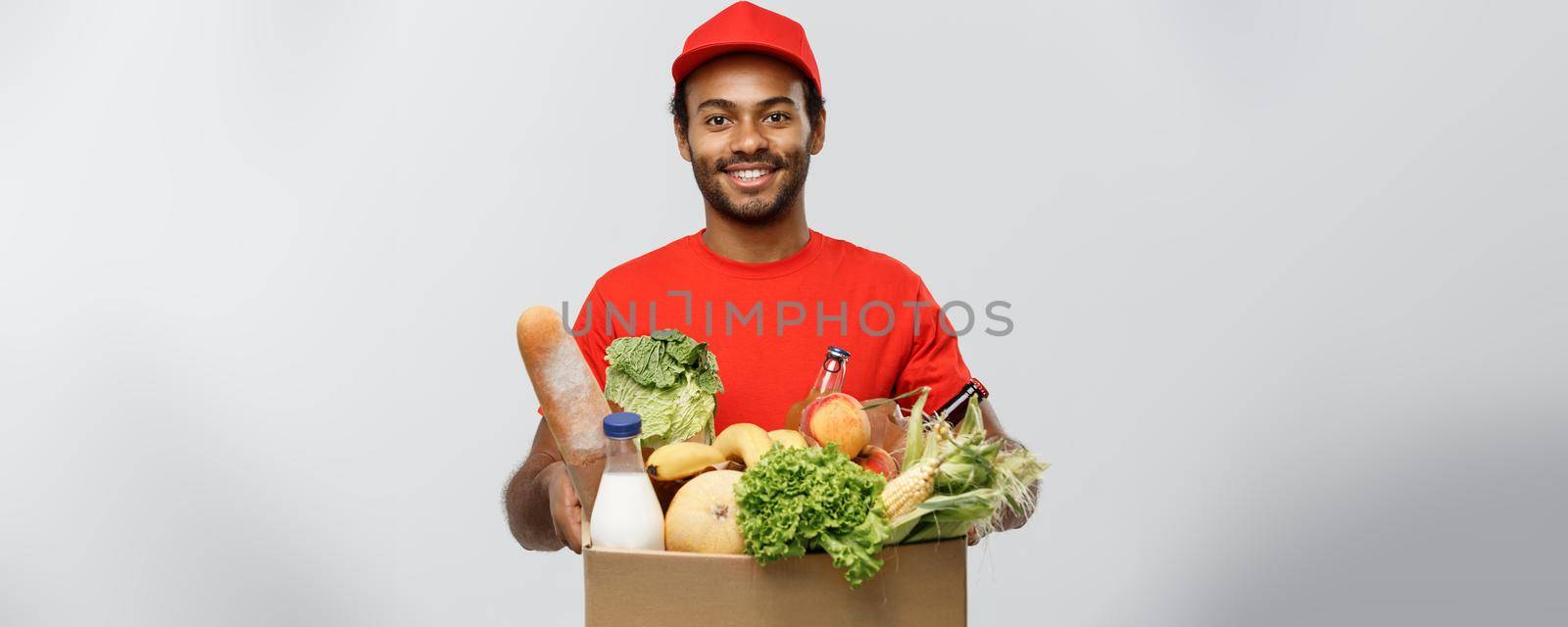 Delivery Concept - Handsome African American delivery man carrying package box of grocery food and drink from store. Isolated on Grey studio Background. Copy Space
