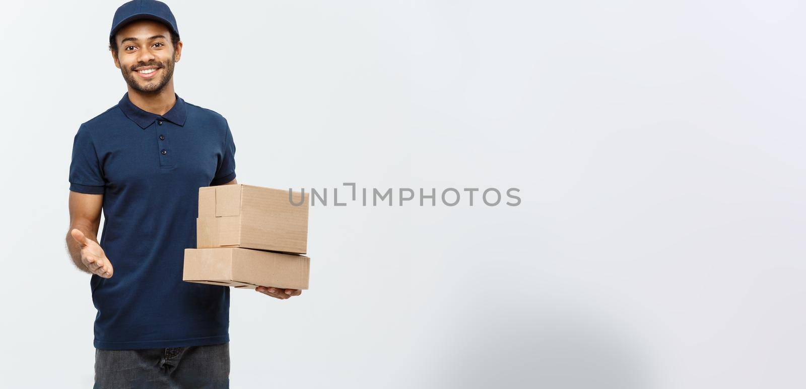 Delivery Concept - Portrait of Happy African American delivery man pointing hand to present box packages. Isolated on Grey studio Background. Copy Space