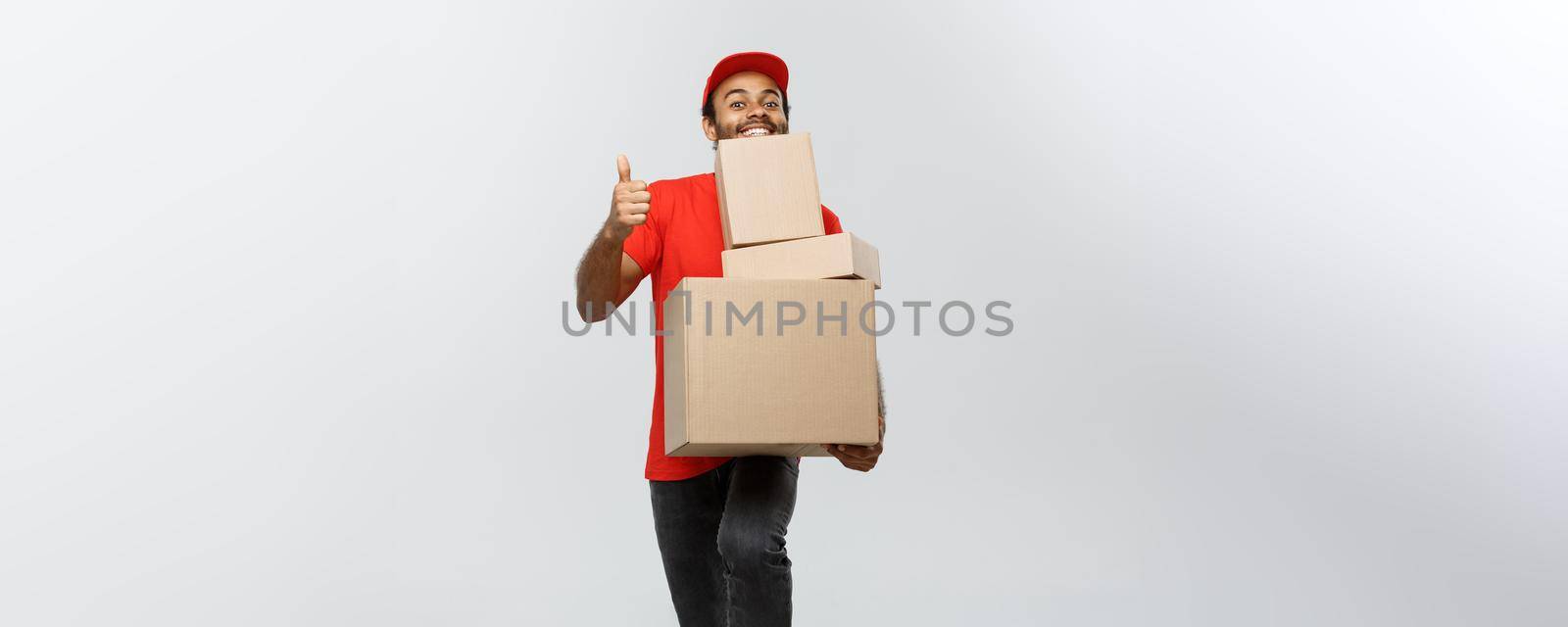 Delivery Concept - Portrait of Happy African American delivery man holding box packages and showing thumps up. Isolated on Grey studio Background. Copy Space