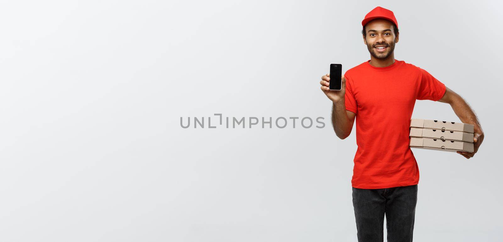 Delivery Concept - Portrait of Handsome African American delivery man or courier with pizza box showing mobile phone on you to check the order. Isolated on Grey studio Background. Copy Space