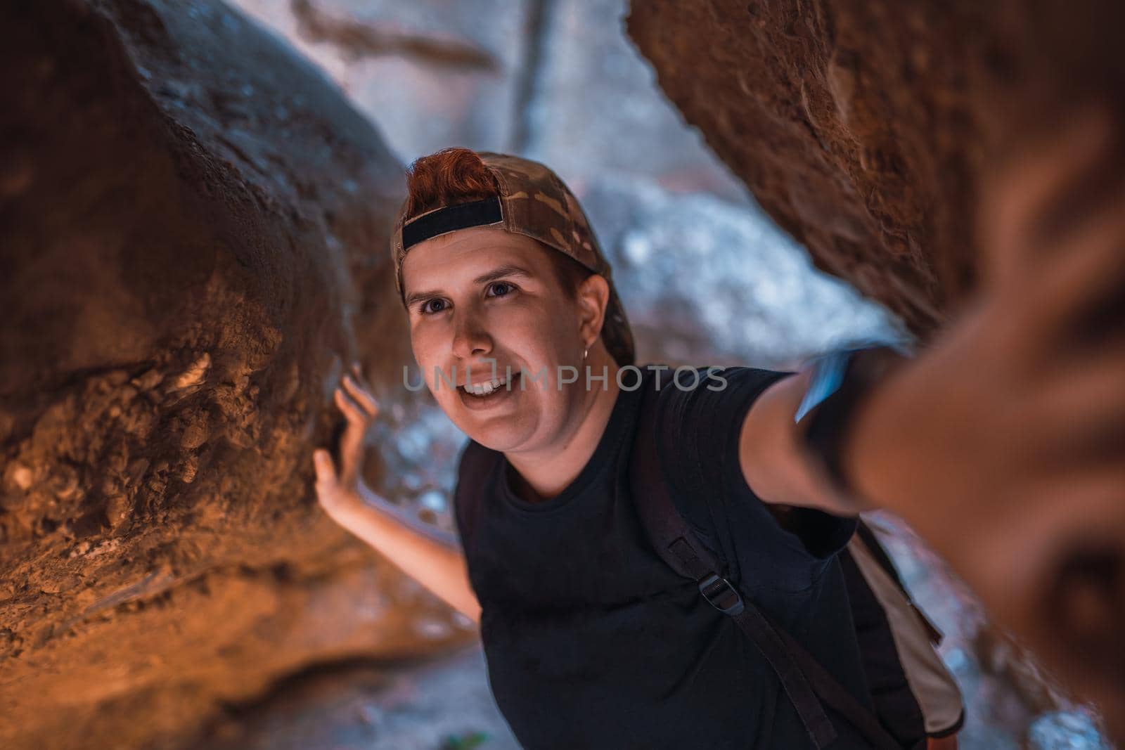 young woman hiking, exploring the entrance of a cave. woman on vacation. young woman hiking in nature. travel person. woman walking in nature. background of a mountain with green plants illuminated by sun rays.