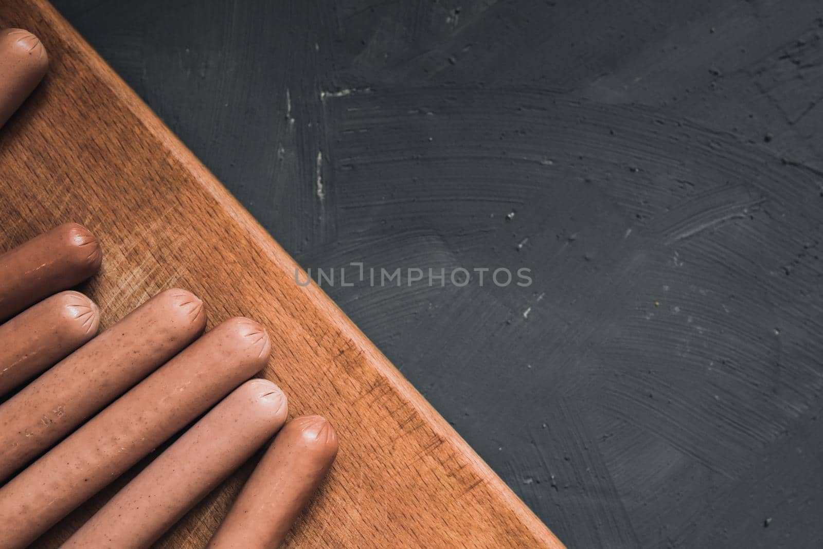 Boiled fried sausages sausages lie on a wooden kitchen board scratched against a dark concrete background.