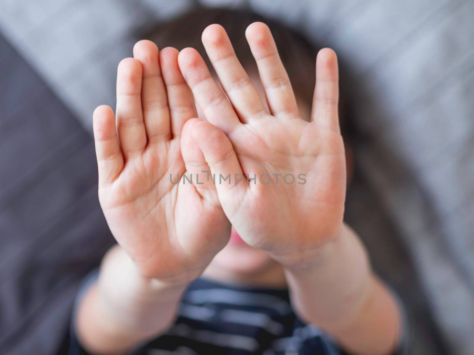 Little boy covers his face with hands. Child refuses to be photographed. Playful kid shows his palm hands instead of laughing face.