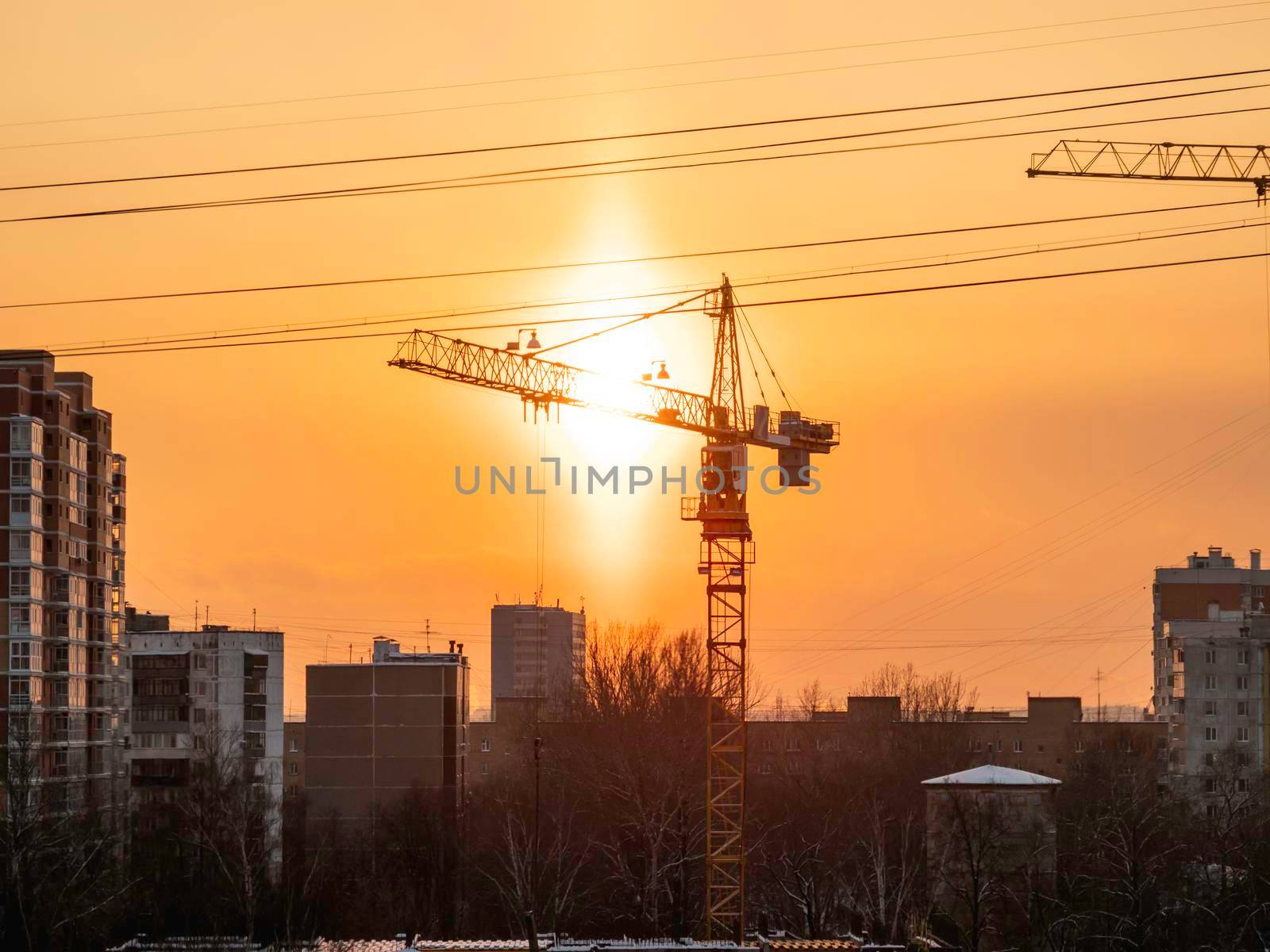 Construction of residential district. Unfinished apartment building with protruding fittings. Silhouettes of walls on the background of an orange sunset.