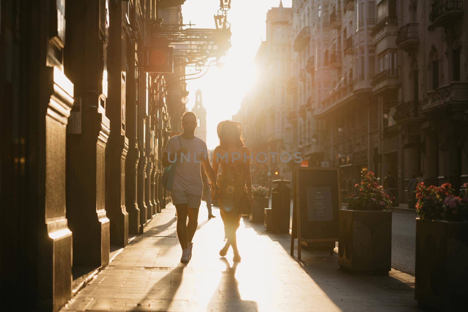 A girl and her boyfriend are walking holding each other's hand in Spain. by RomanJRoyce