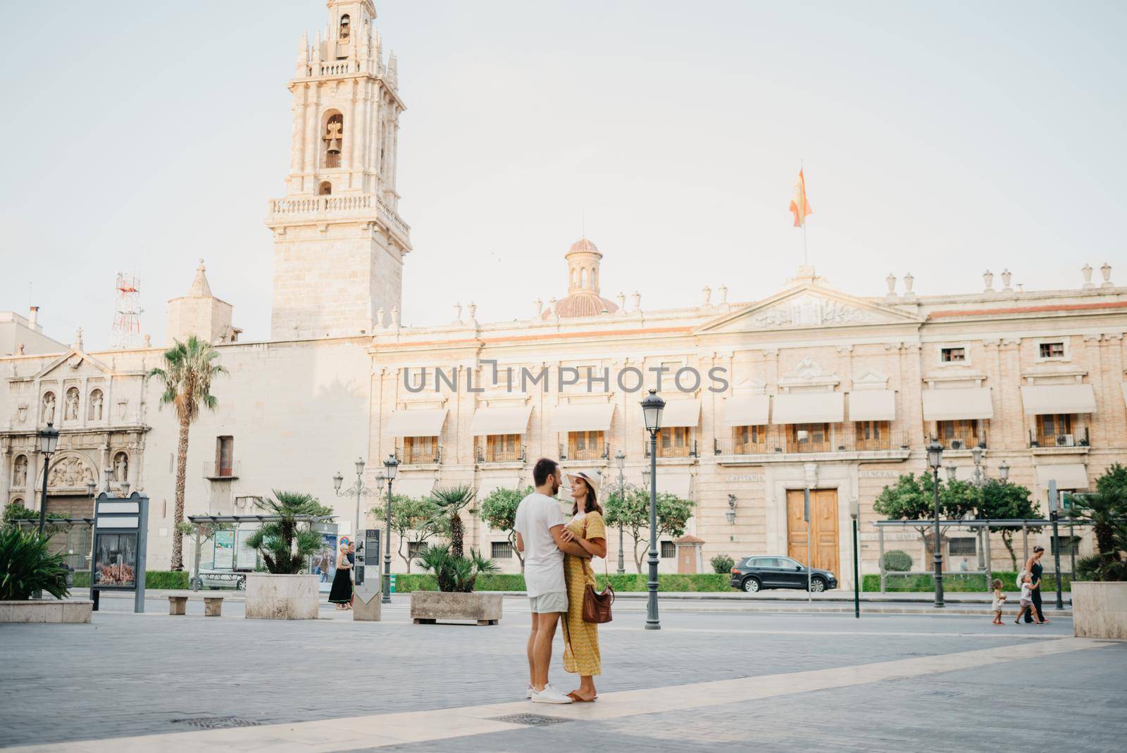 A girl in a hat and a dress with a plunging neckline is dancing with her boyfriend with a beard and sunglasses in the old town. A couple of tourists on the sunset in Valencia.