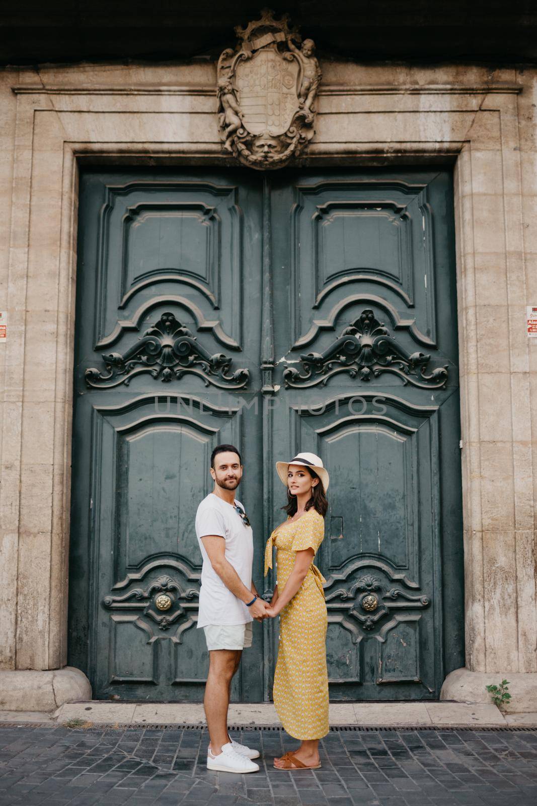 A girl and boyfriend are staying near the giant doors holding each other's hand. by RomanJRoyce