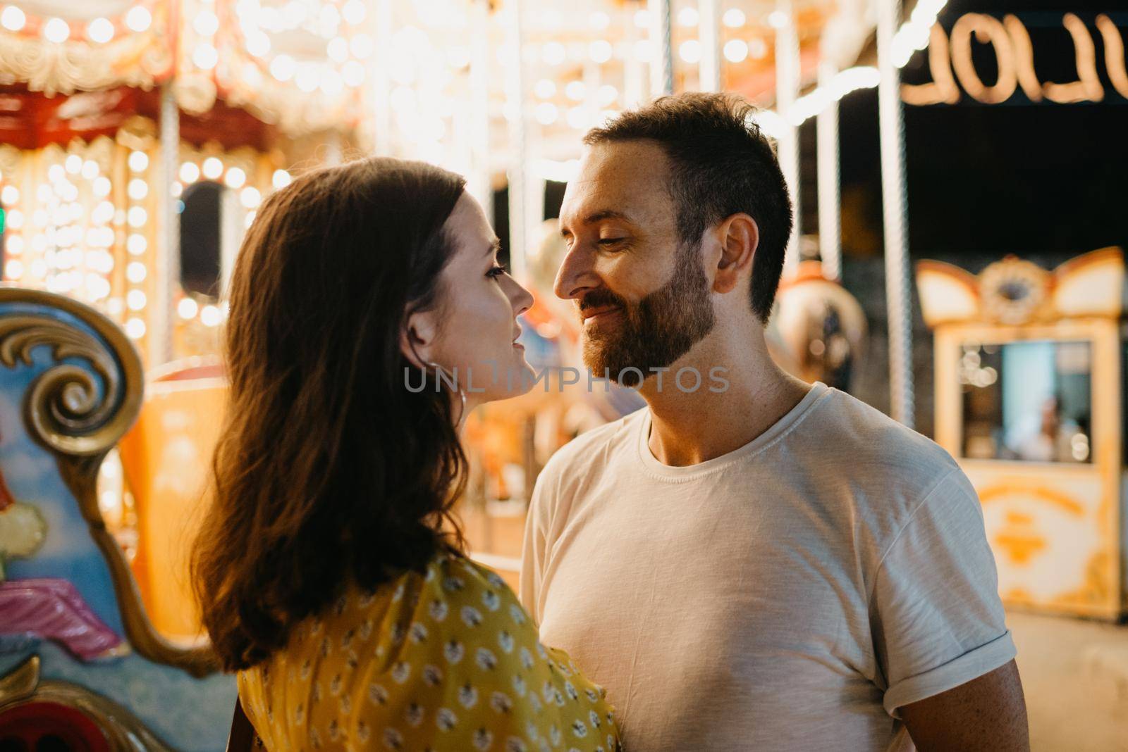 A woman in a yellow dress with a plunging neckline and a man with a beard are admiring of each other between amusement rides. A couple of lovers on a date at the fair in Valencia.