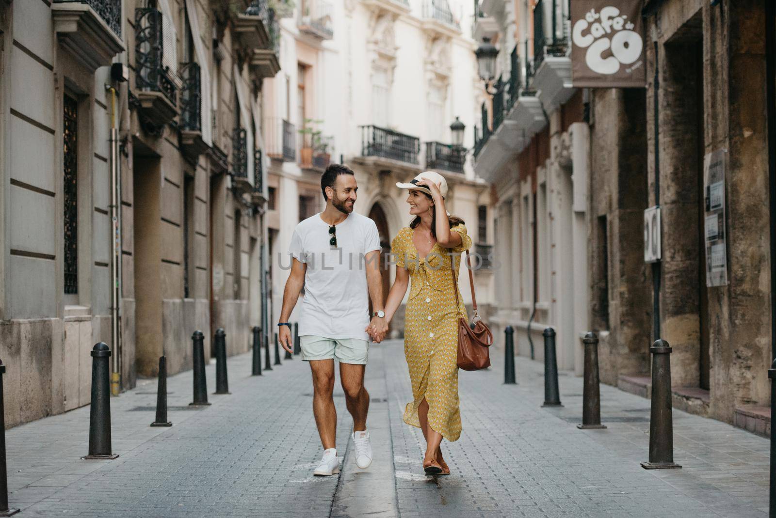 A girl in a hat and a yellow dress and her boyfriend with a beard are walking by RomanJRoyce