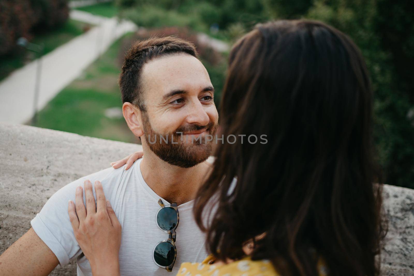 A close photo of a man with beard who is hugging a brunette girl in a yellow dress who on the ancient bridge in old Spain town. A couple of tourists on a date in Valencia.
