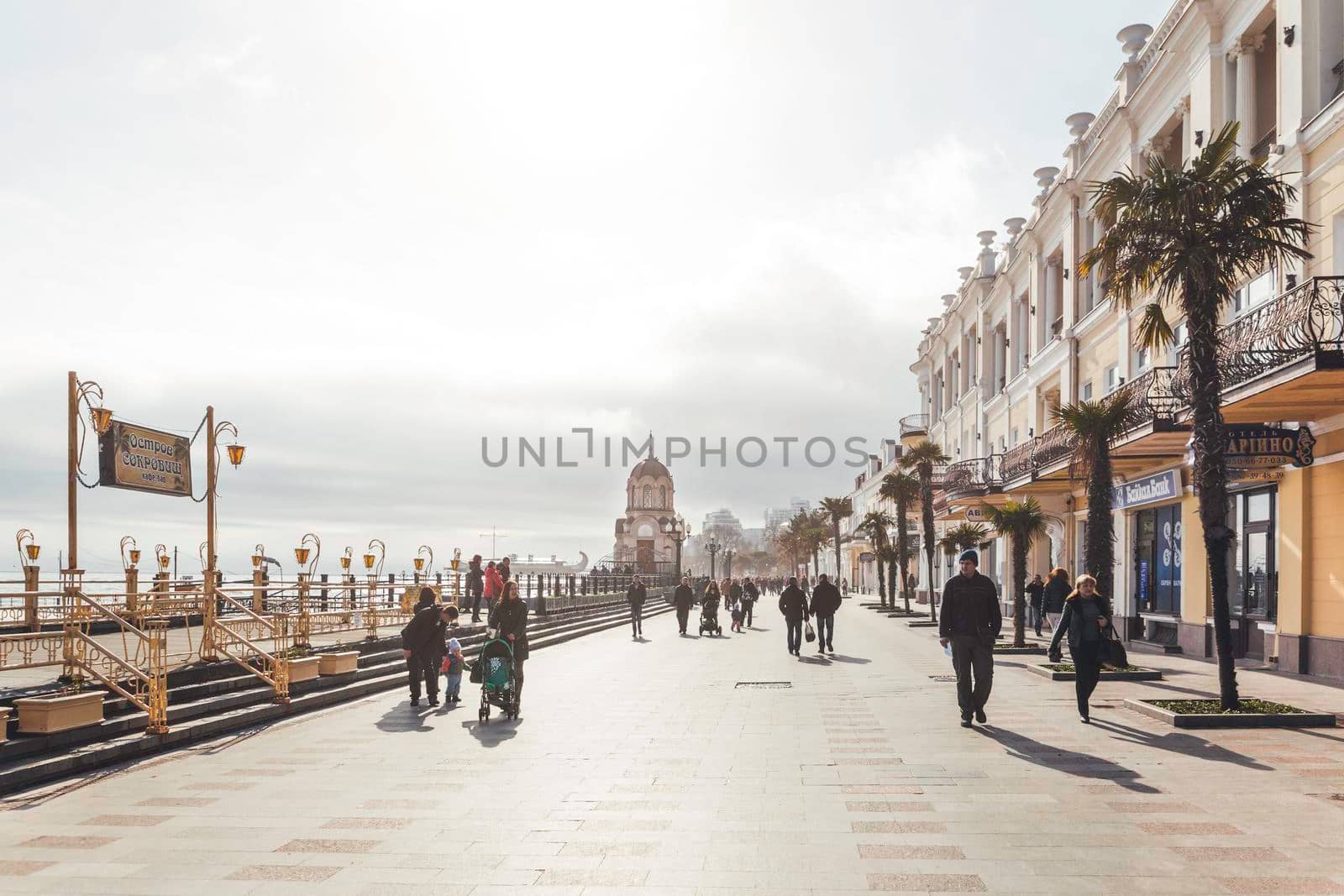 YALTA, CRIMEA - February 05, 2015. Local people and tourists walk along Black sea embankment. Cobbled street with stores and cafes. by aksenovko