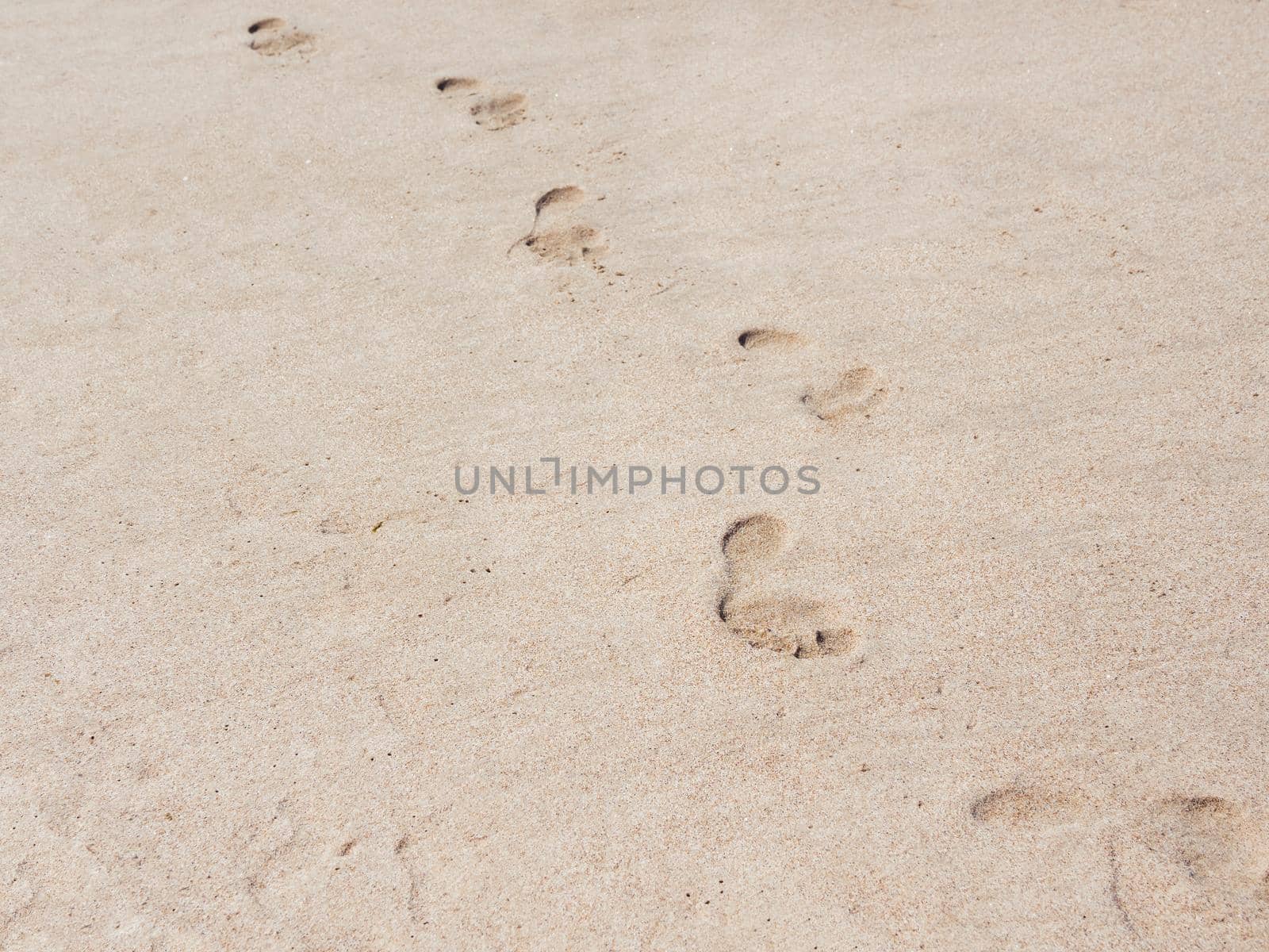 Male footprints on a sandy beach. A chain of bare footprints. Trail to follow. Outline of feet tracks.