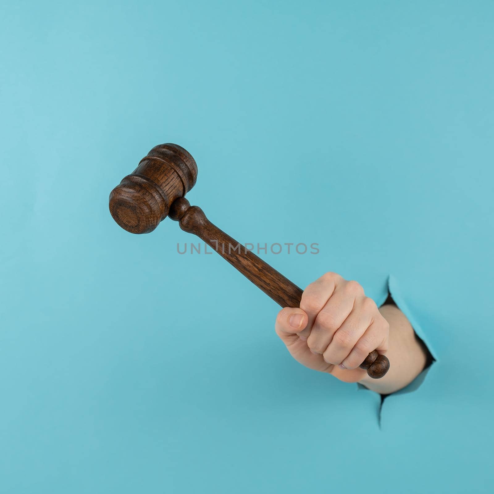 A woman's hand with a wooden judge's gavel sticks out of a hole in a blue background. by mrwed54