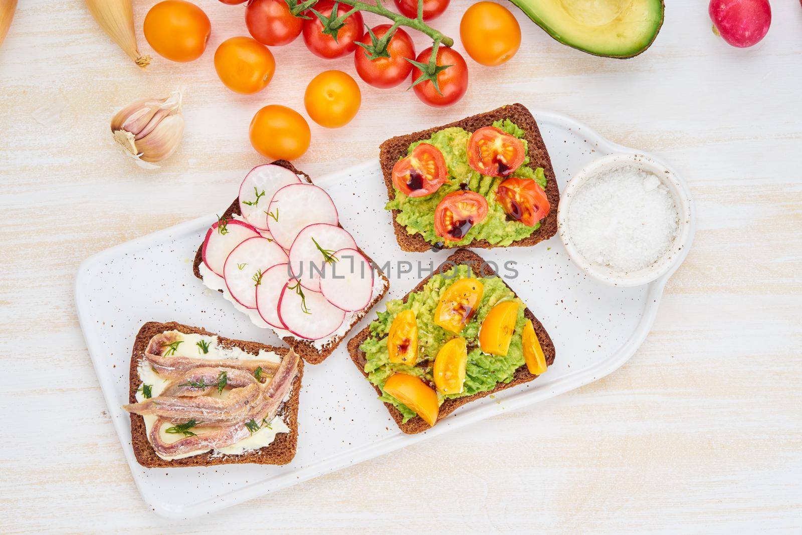 Set of smorrebrods with fish, anchovies, avocado, tomatoes, radish. Top view, white board, white background