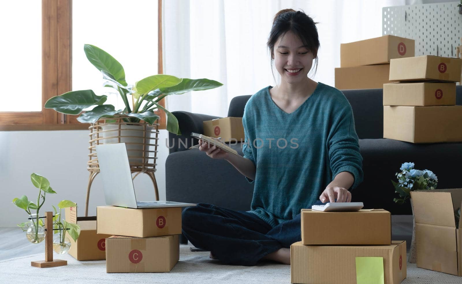 Asian women write note of orders of goods with a smiling face in concept of sme, e-commerce business.