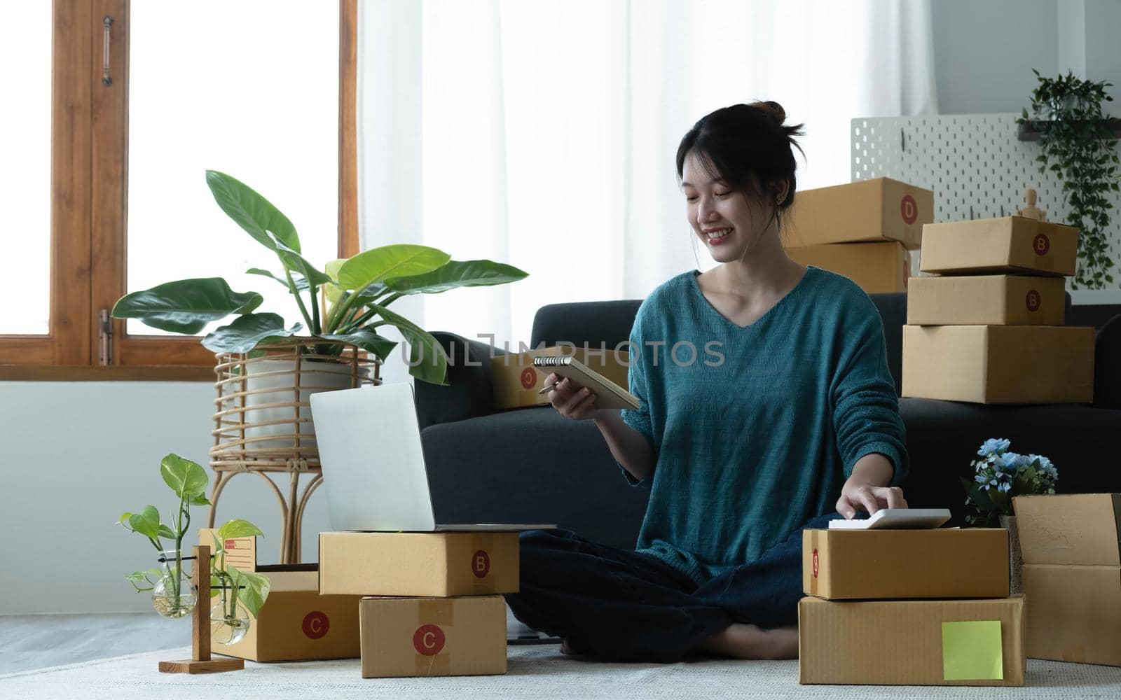 Asian women write note of orders of goods with a smiling face in concept of sme, e-commerce business by wichayada