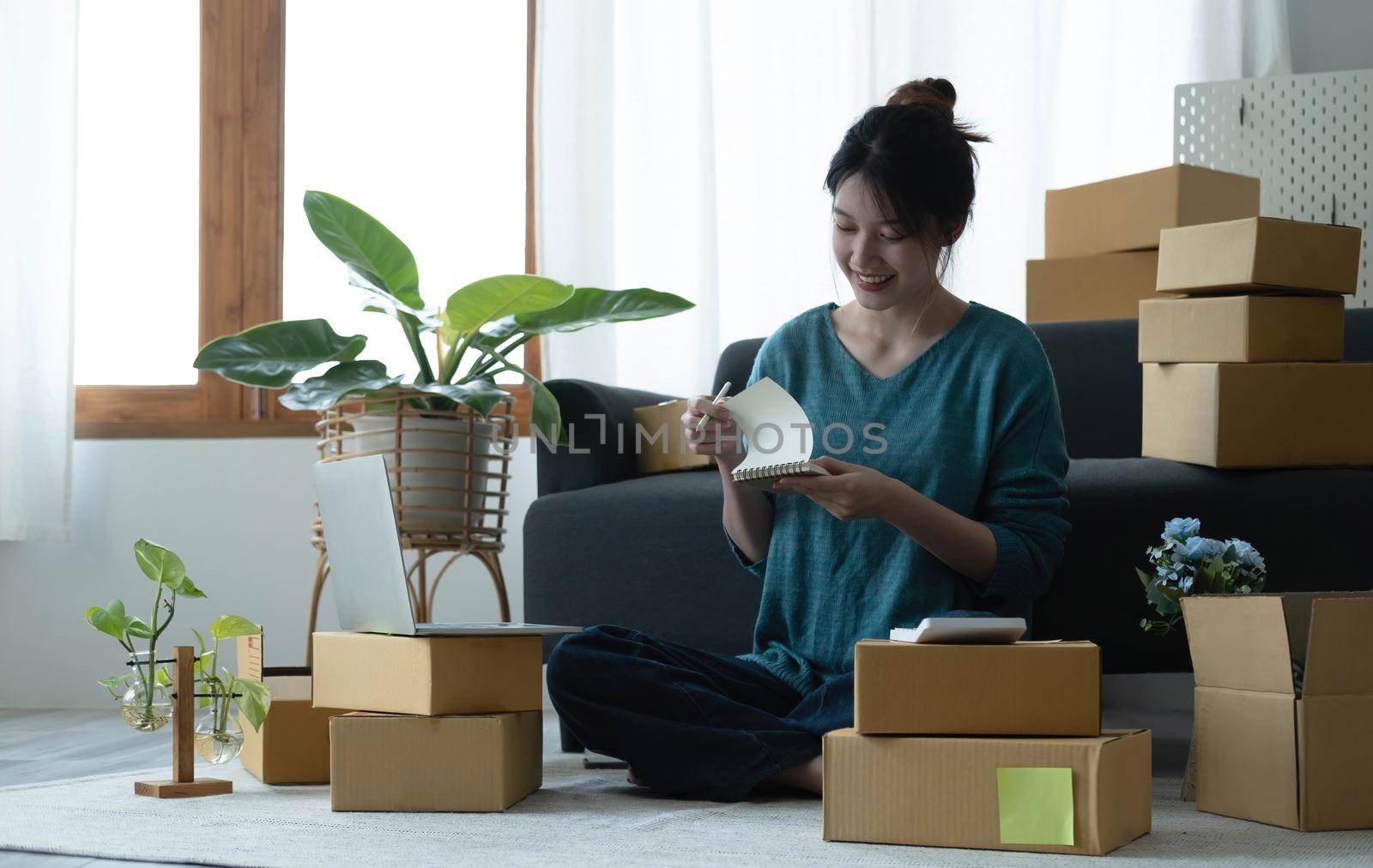 Asian women write note of orders of goods with a smiling face in concept of sme, e-commerce business.