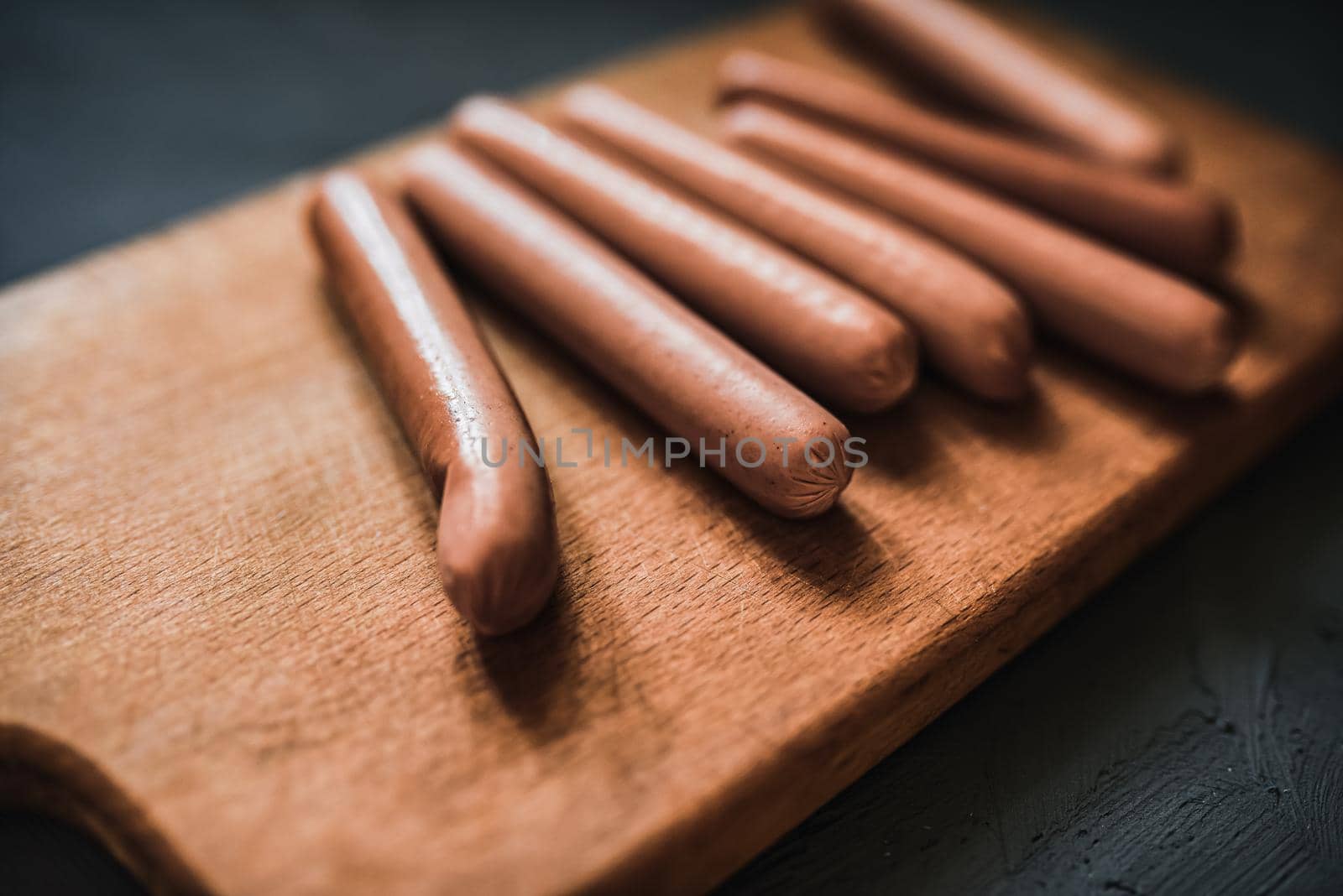 Boiled fried sausages sausages lie on a wooden kitchen board scratched against a dark concrete background.