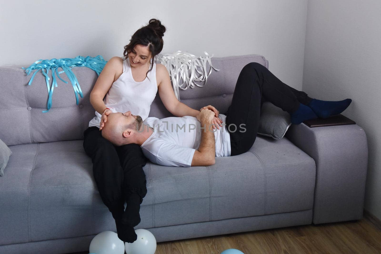 Photo of cheerful romantic caucasian family couple smiling and hugging while sitting on sofa at home. Man and woman in love