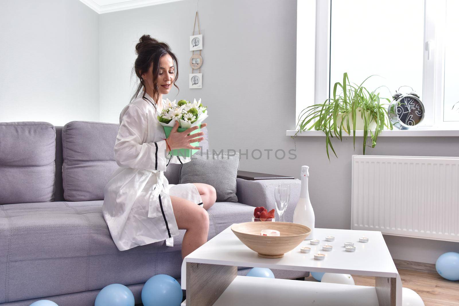 Beautiful brunette woman dressing gown with bouquet indoors. Female portrait in living room
