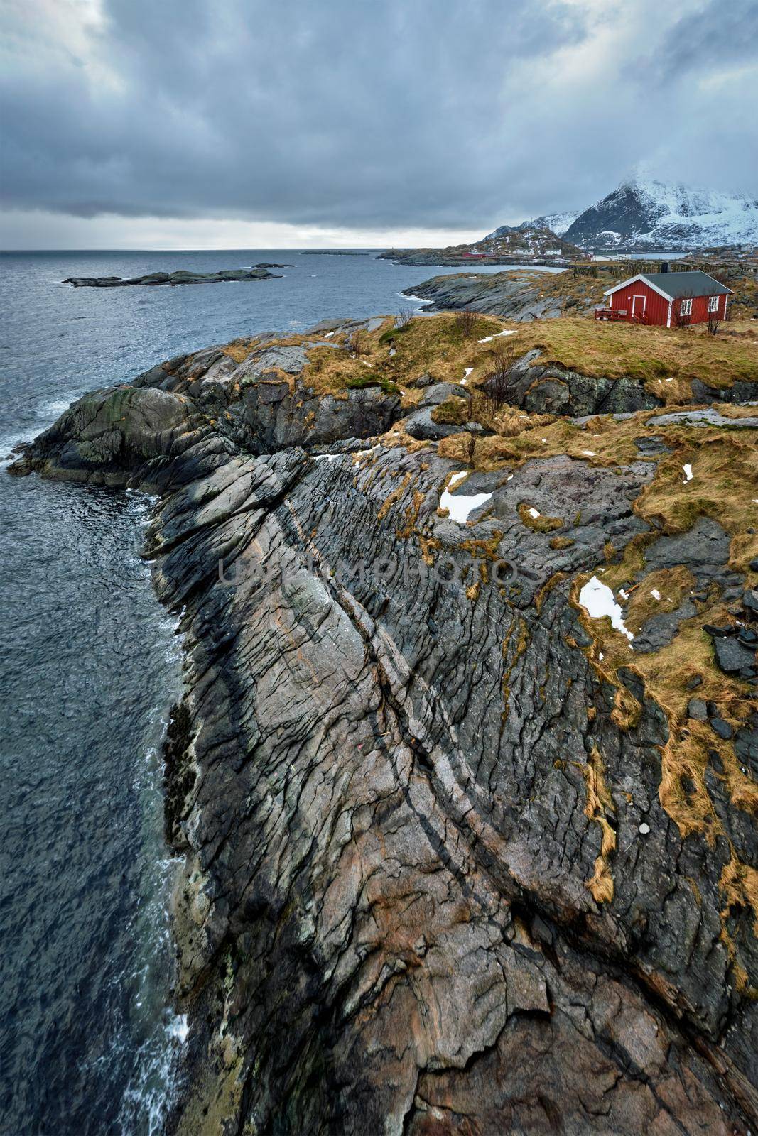 Clif with traditional red rorbu house on Litl-Toppoya islet on Lofoten Islands, Norway in winter