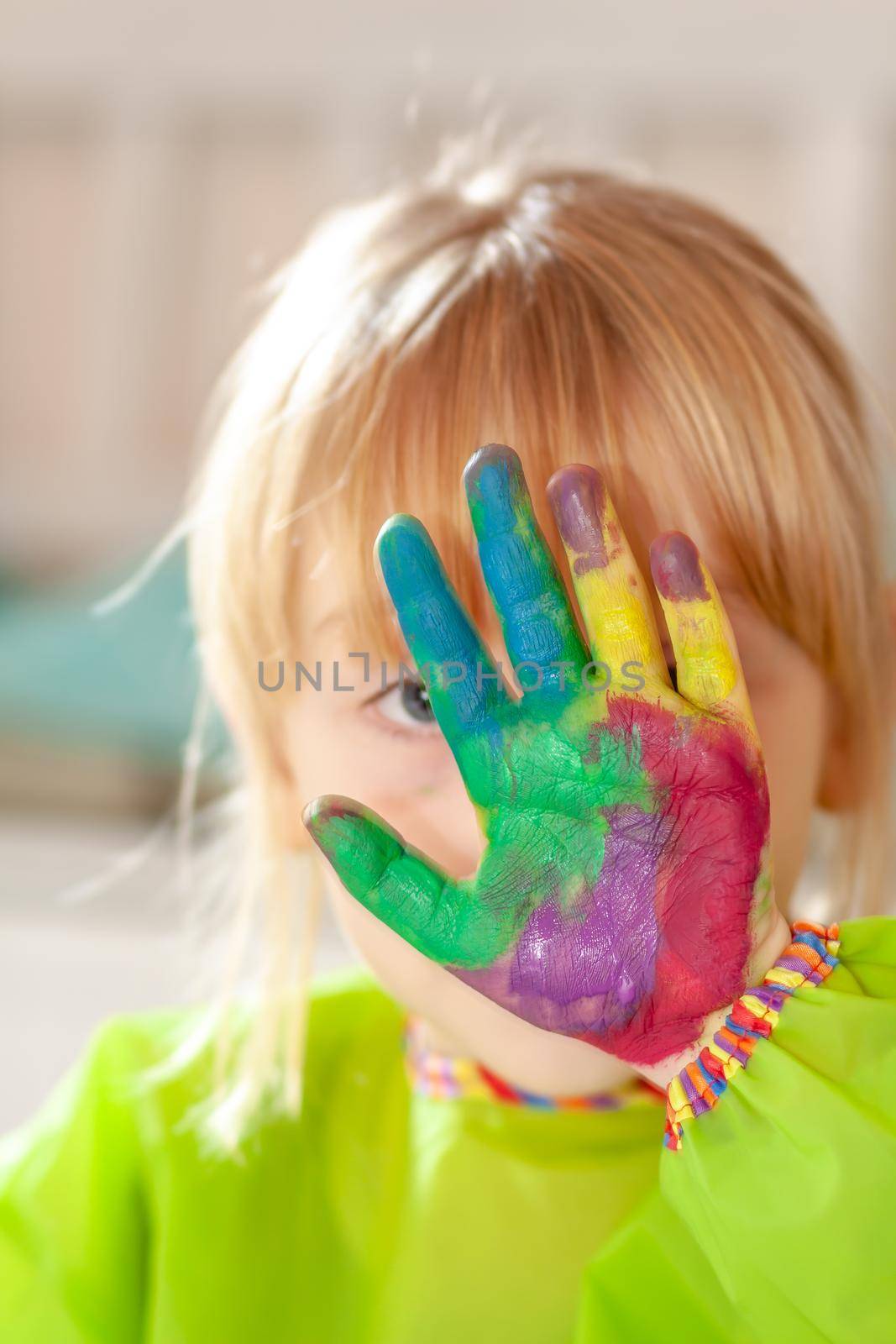 Little girl hiding behing her watercolour painted hand at home during the pandemic lockdown.