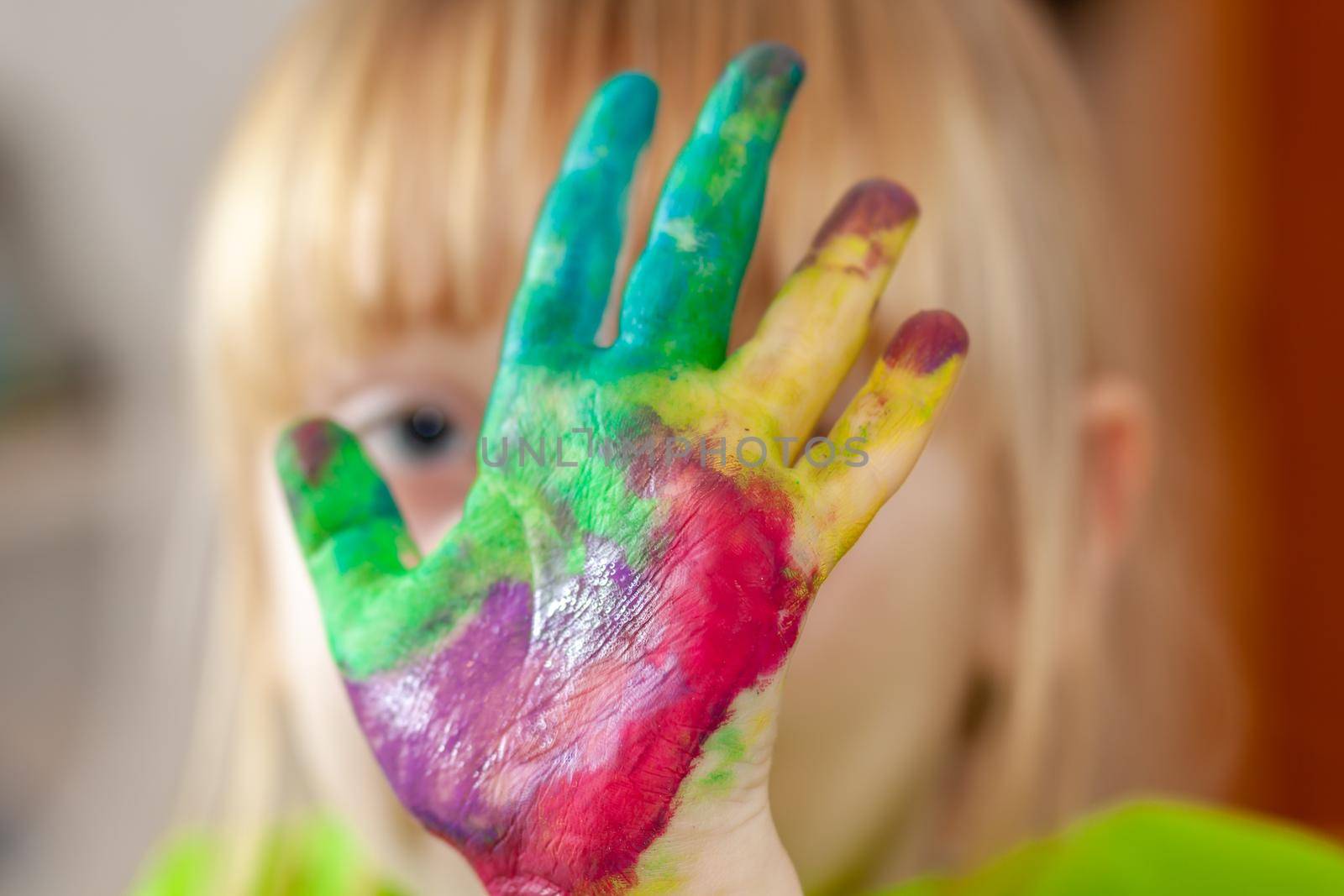 Little girl hiding behing her watercolour painted hand at home during the pandemic lockdown.