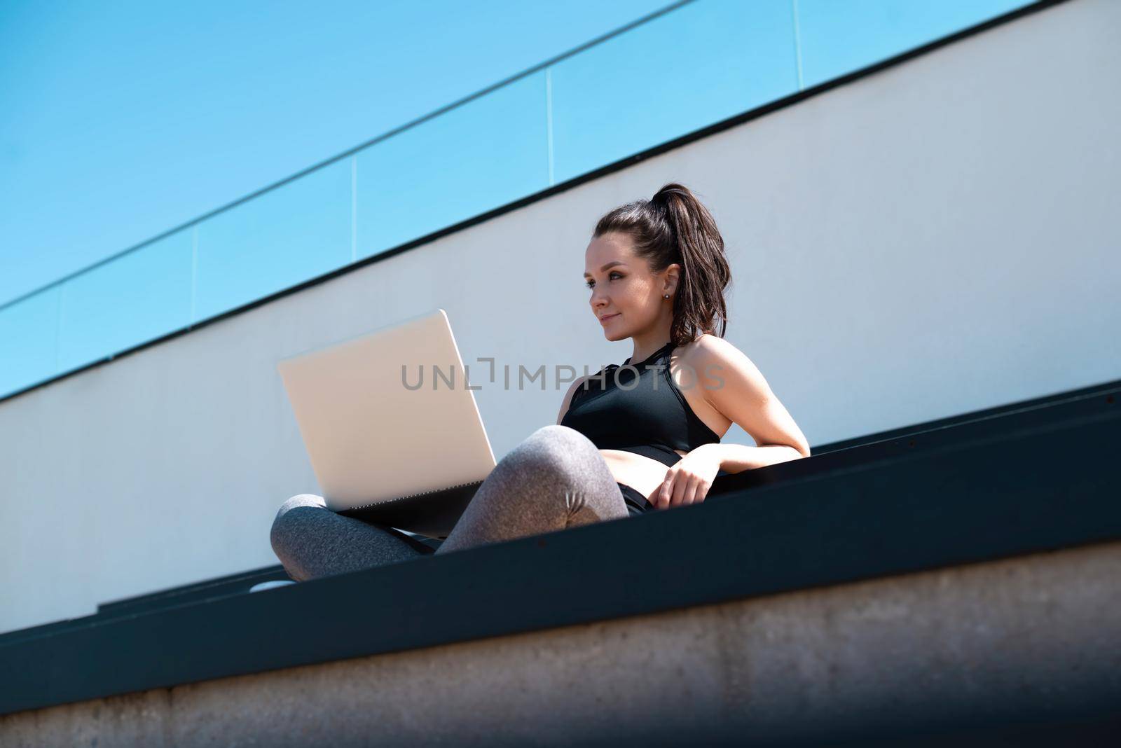 girl in sportswear on a summer outdoor sports field is sitting with a laptop