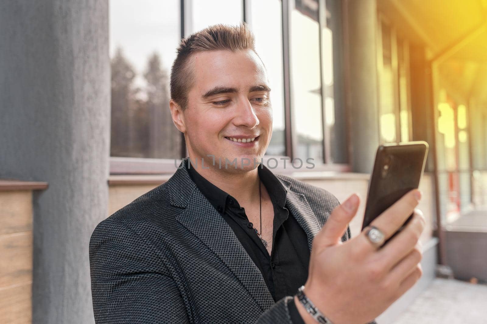 Portrait of a smiling, cheerful man of Caucasian appearance of a businessman in a jacket and shirt with a mobile phone in his hands on the street outdoor.