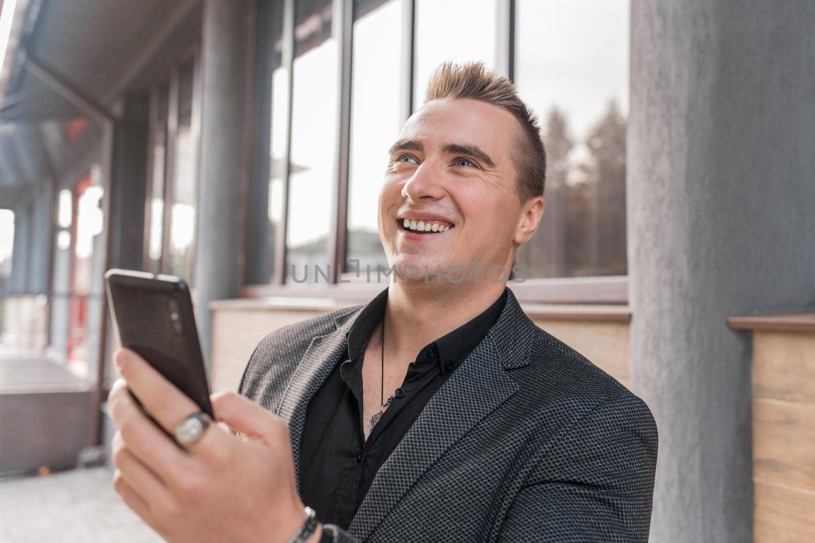 Portrait of a smiling, cheerful man of Caucasian appearance of a businessman in a jacket and shirt with a mobile phone in his hands on the street outdoor.