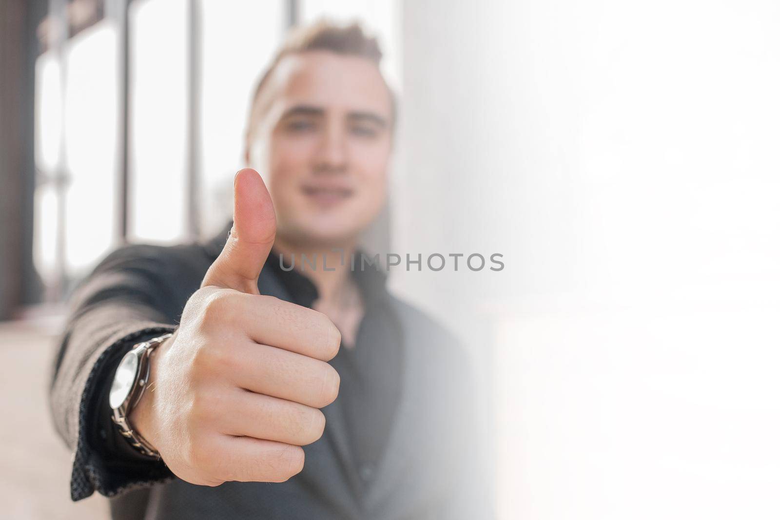 A young man shows a close-up of a thumbs up class against a street outdoor background.
