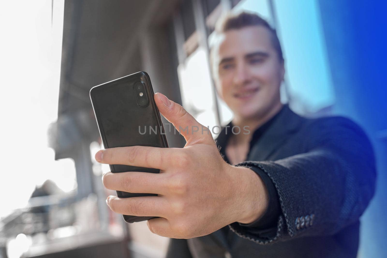 A young satisfied guy holds a smartphone or mobile phone in his hand, takes a selfie or talks on video on the outdoor street, close-up.