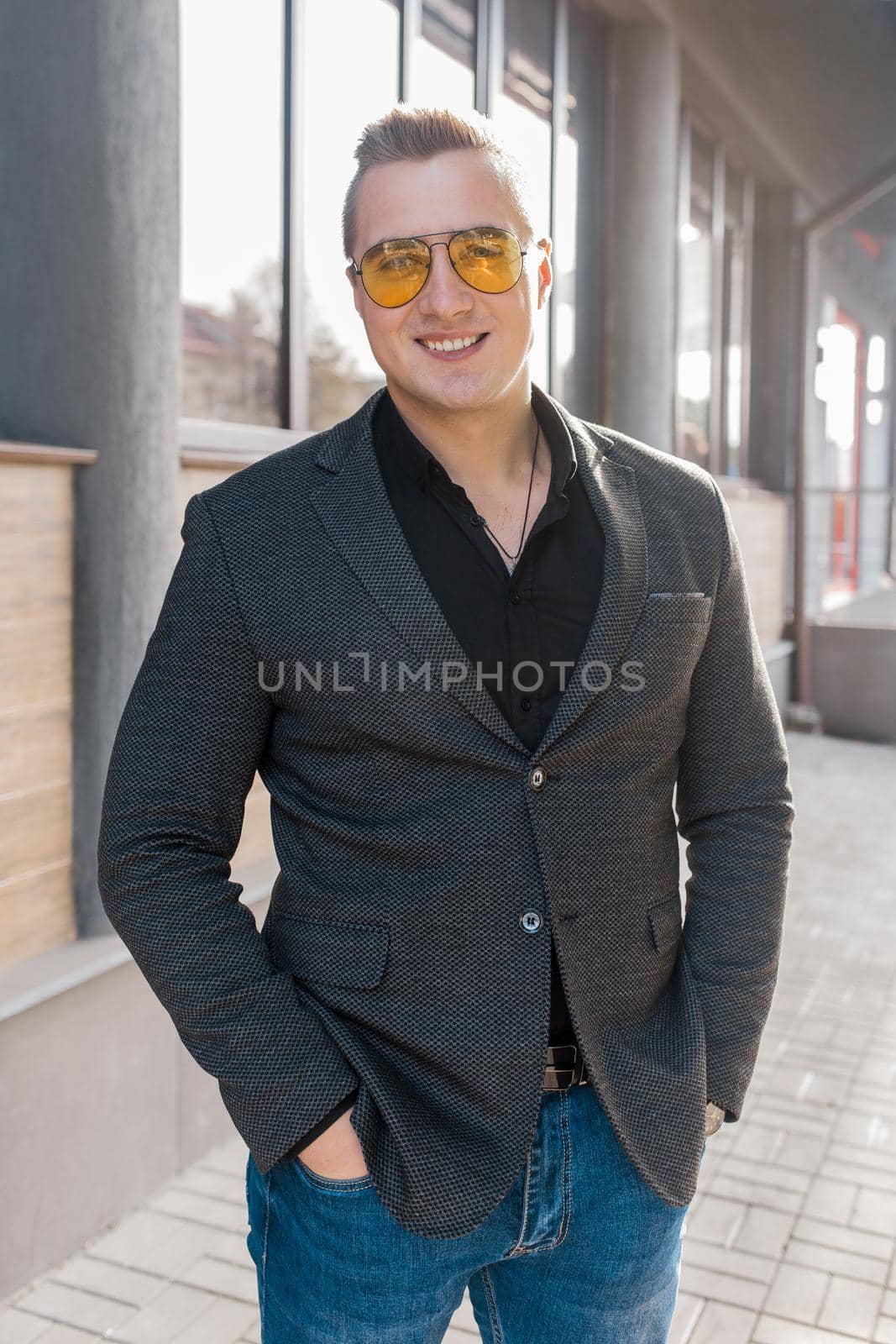 Stylish positive young attractive guy of European appearance businessman portrait in jacket, shirt and jeans, in sunglasses on the street outdoor.