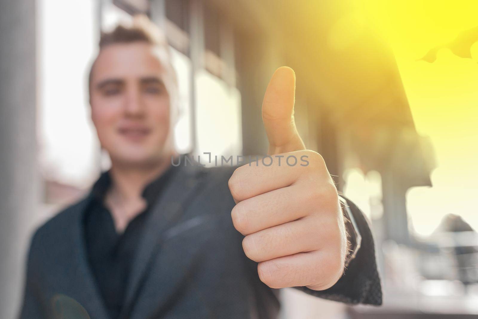 A young man shows a close-up of a thumbs up class against a street outdoor background.