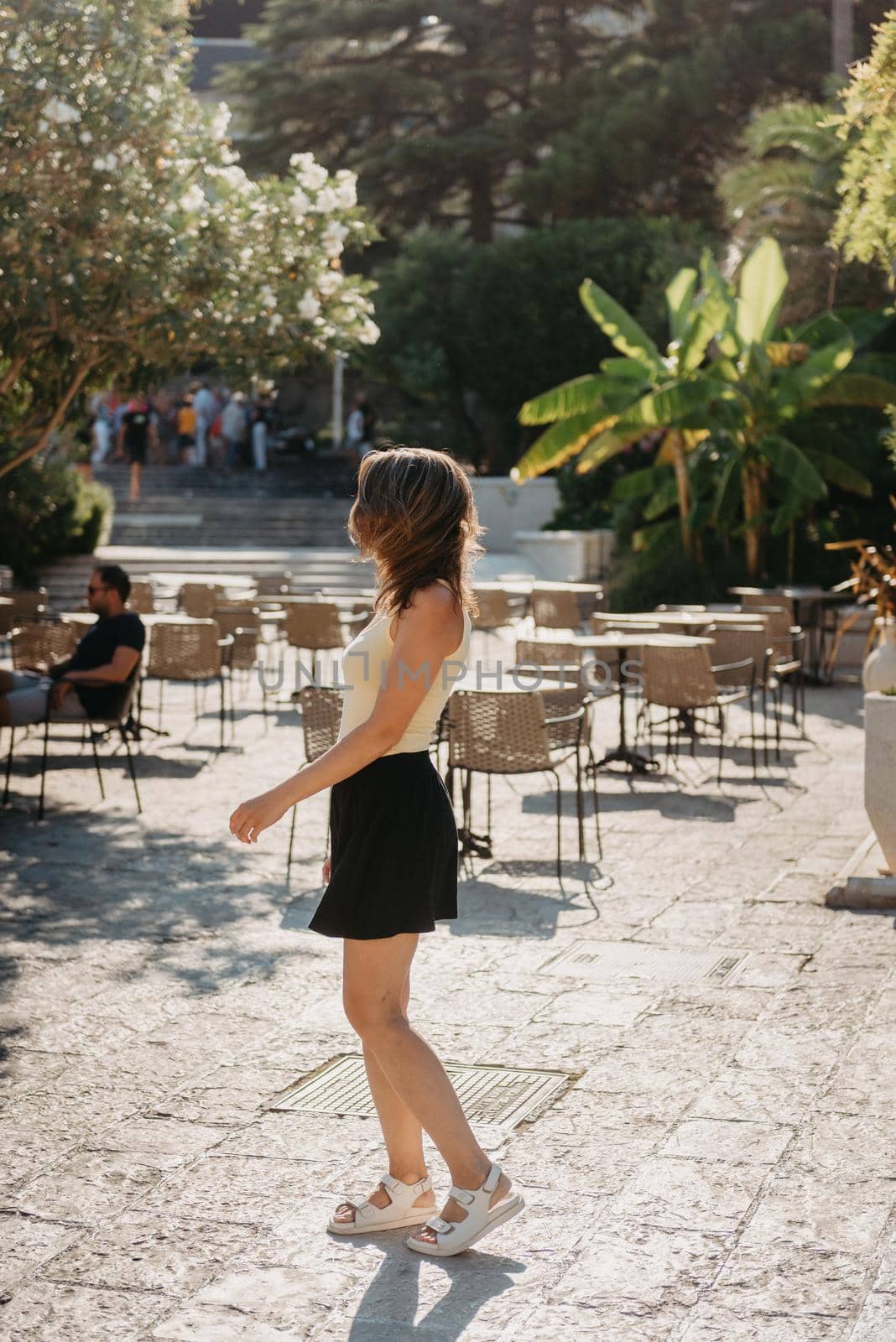 Girl tourist walking through ancient narrow street on a beautiful summer day in MEDITERRANEAN MEDIEVAL CITY , OLD TOWN bUDVA, MONTENEGRO. Young beautiful cheerful woman walking on old street at tropical town. Pretty girl looking at you and smiling