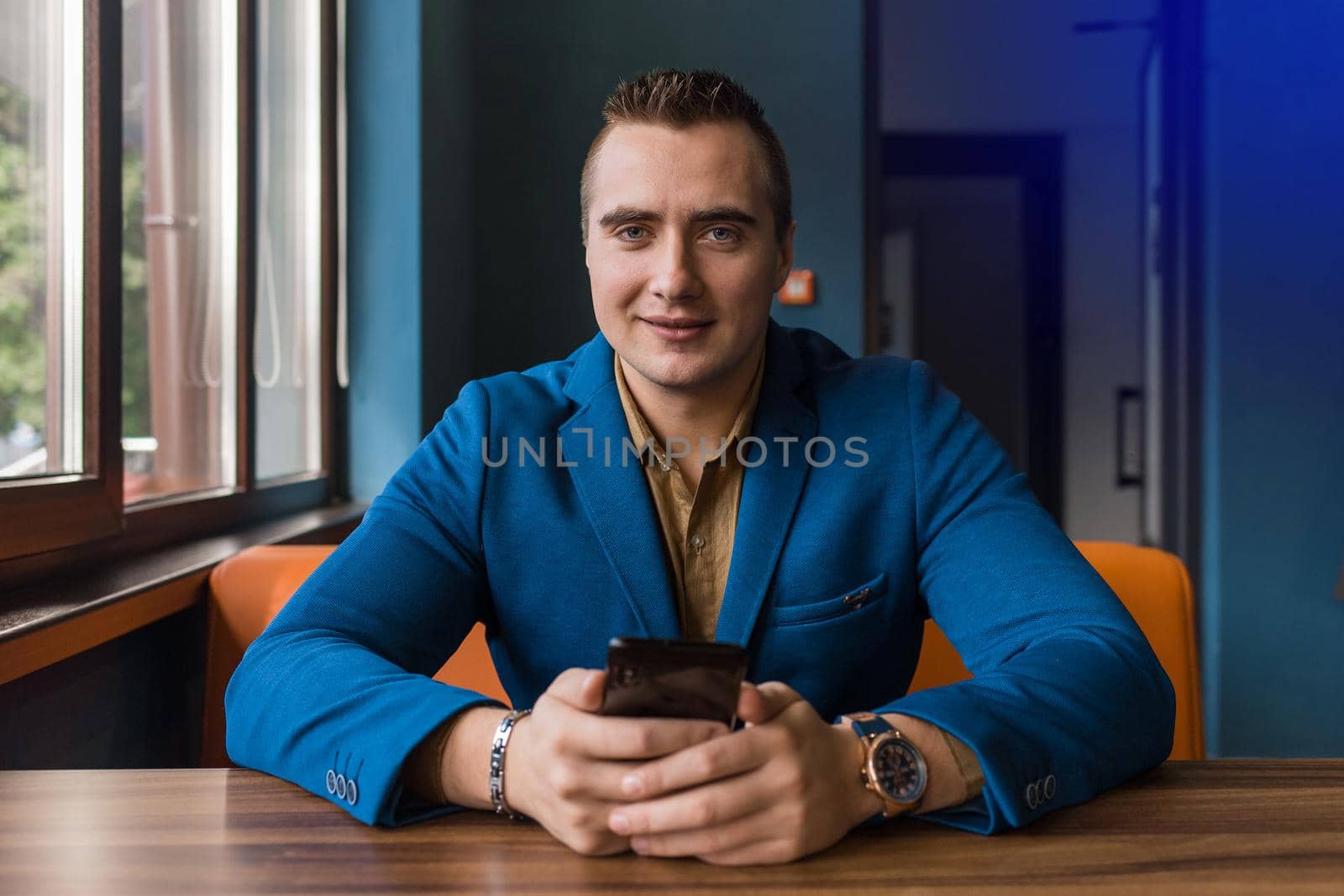 Stylish young, businessman of European appearance portrait of a man in a jacket and shirt sits at a table and uses a mobile phone in a cafe.