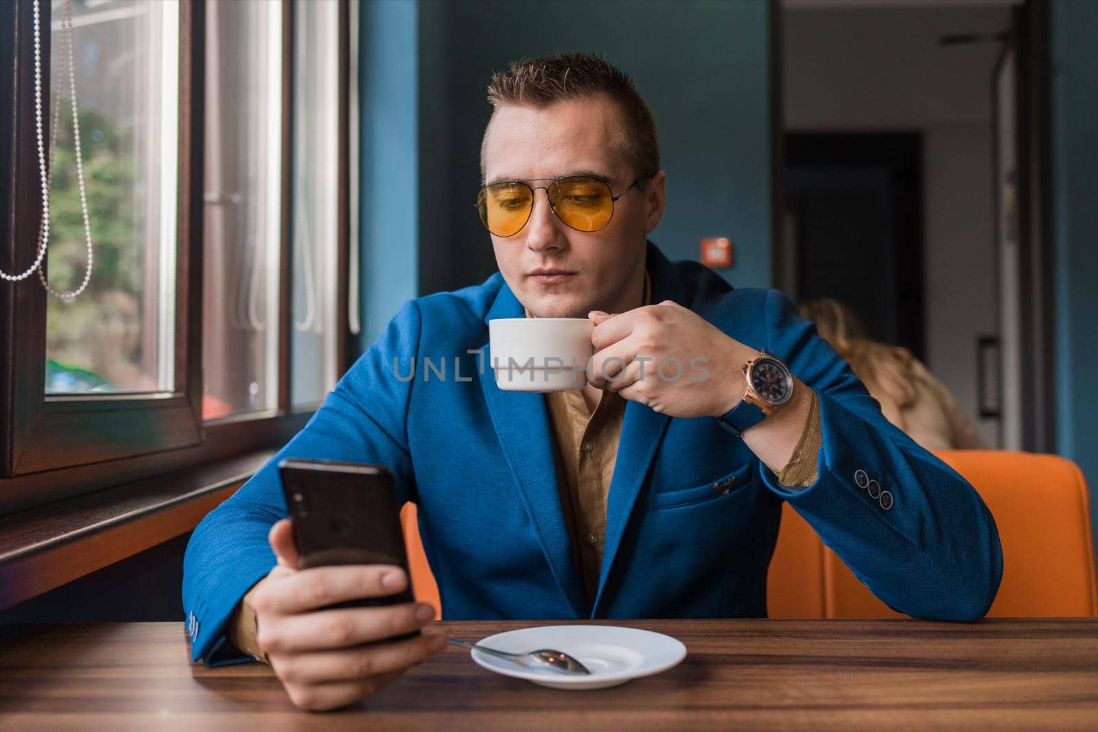 A young handsome guy businessman of European appearance portrait, uses a smartphone or mobile phone sitting in a cafe at a table on a coffee break.