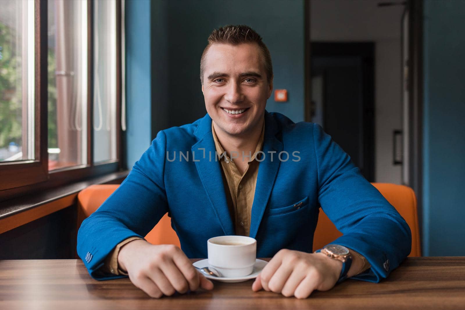 A adult, businessman portrait of Caucasian appearance in a jacket and shirt sits at a table in a cafe with a cup of coffee on a break.