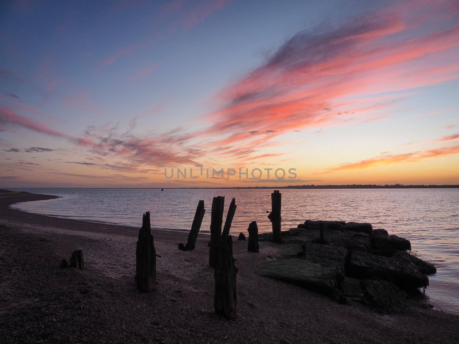 Remains of the old wooden jetty looking out over the sea towards Harwich with a stunning sunset of clouds lit up orange and red, Felixstowe, Suffolk, UK