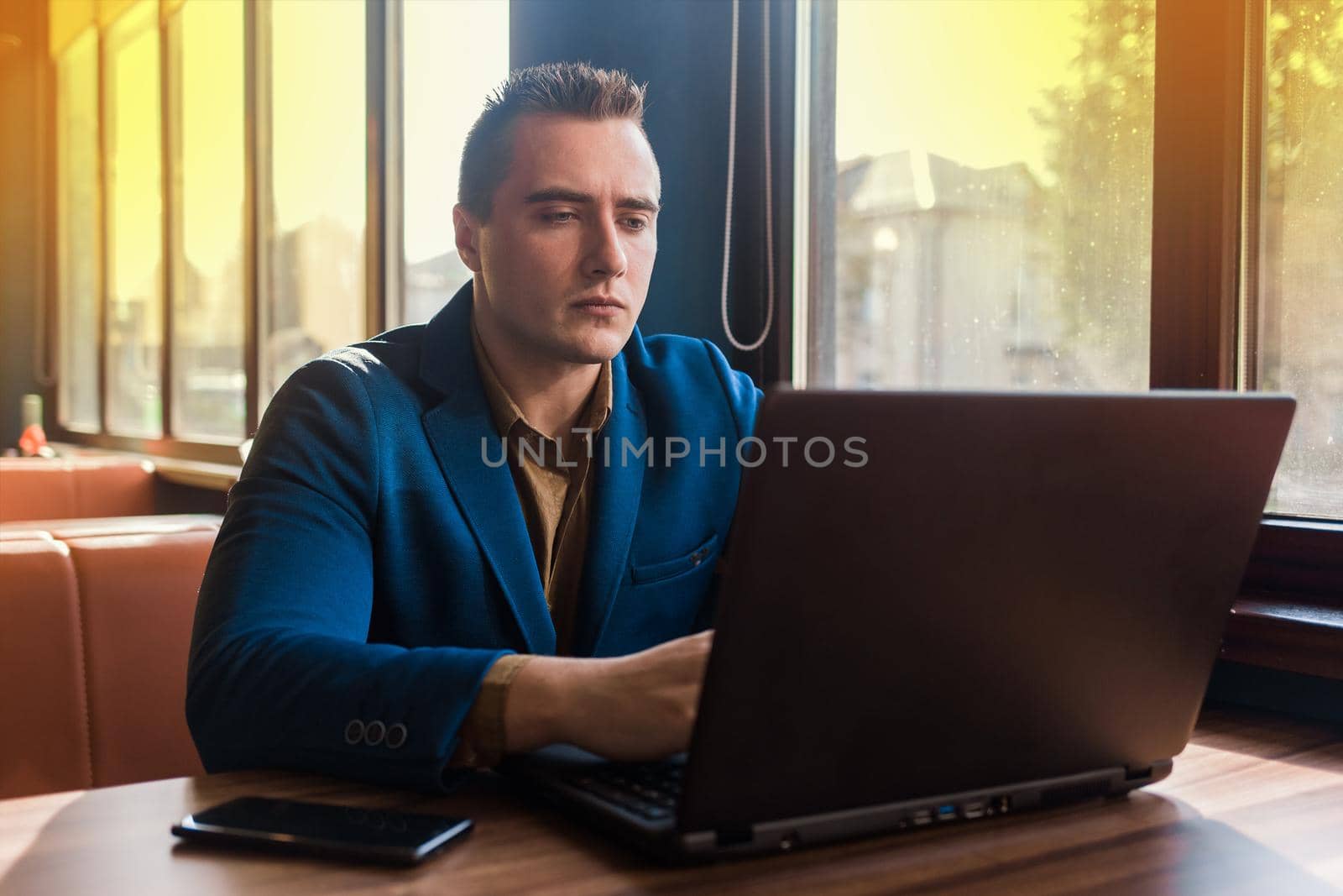 A business man businessman a stylish portrait of Caucasian appearance in a jacket and shirt, works in a laptop or computer, sitting at a table by the window in a cafe.