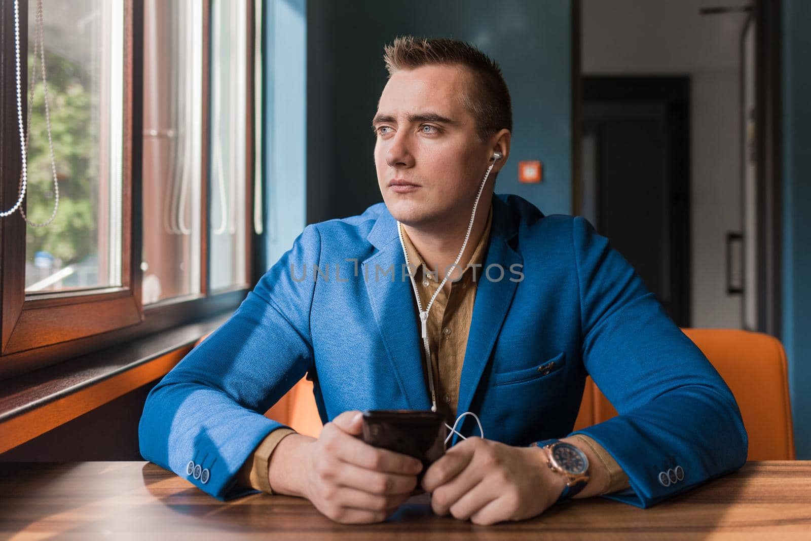 Businessman, a stylish, handsome guy of Caucasian appearance portrait in a suit spends time in a smartphone or mobile phone sitting at a table in the cafe and looking out the window background.