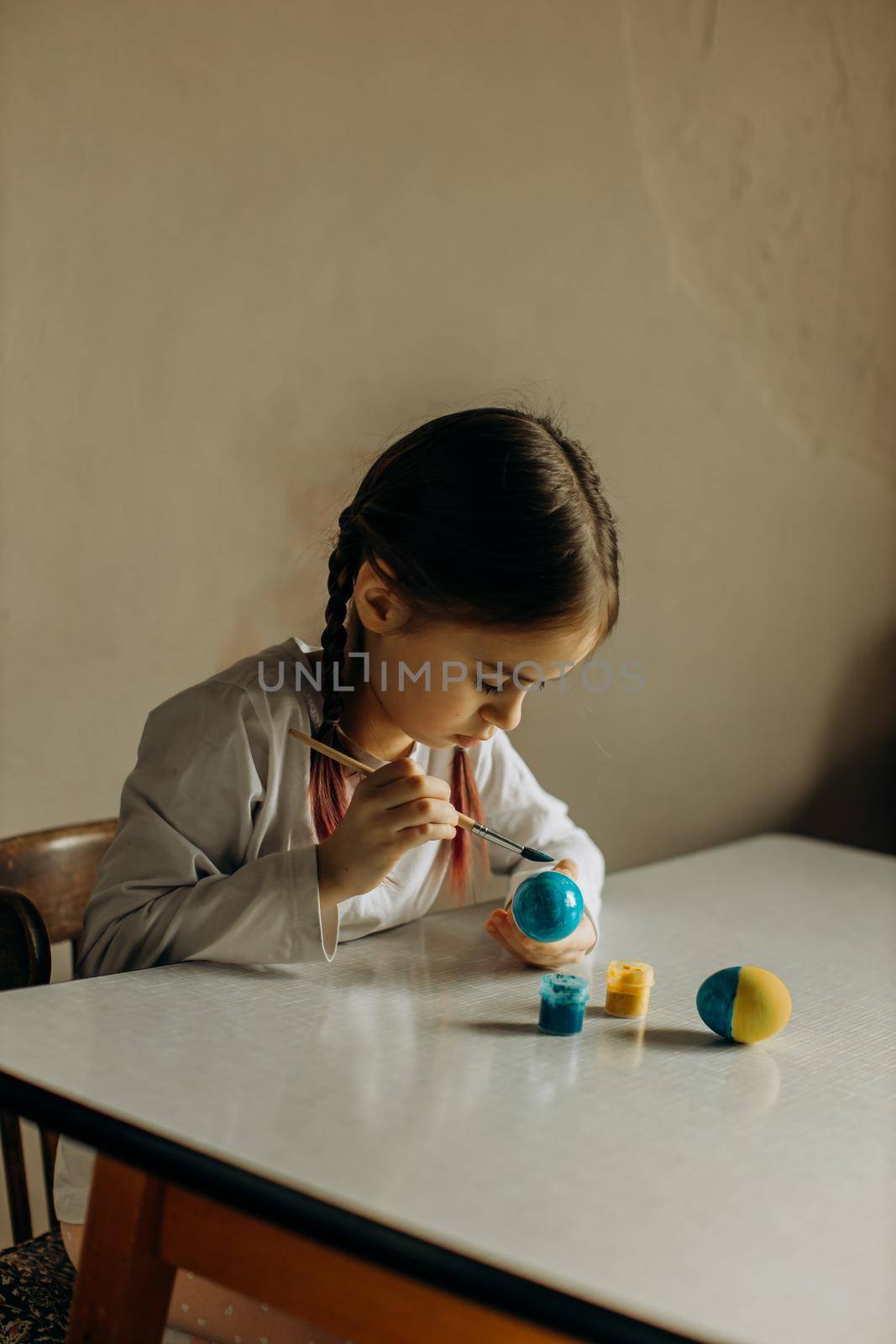 Cute little child girl painting with blue and yellow colors Easter eggs. Hands of a girl with a easter egg. Close-up. by Mihova