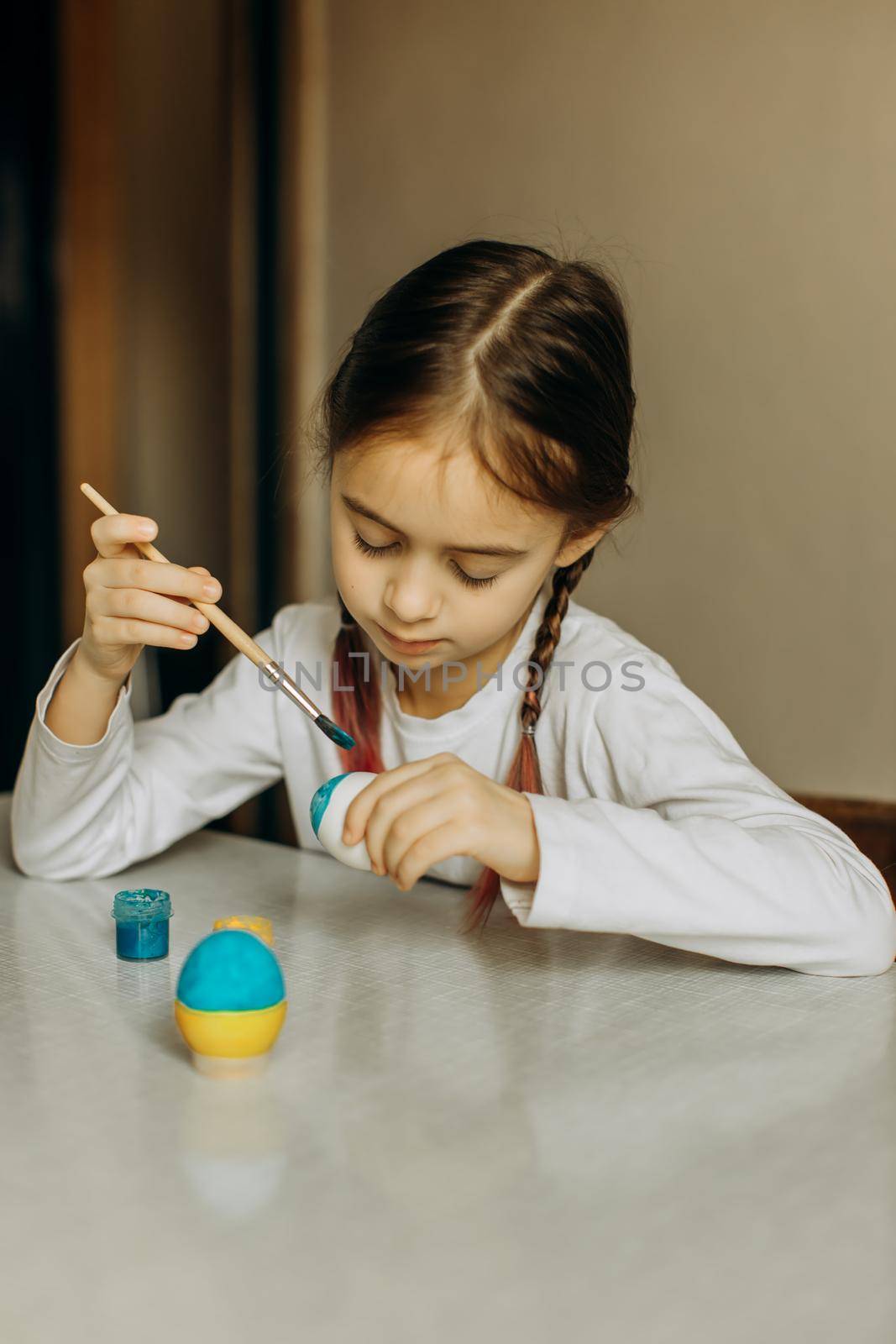 Portrait of a Ukrainian girl. the child paints the egg blue and yellow. The child loves and supports his country. Cute little child girl painting with blue and yellow colors Easter eggs. Hands of a girl with a easter egg. Close-up.