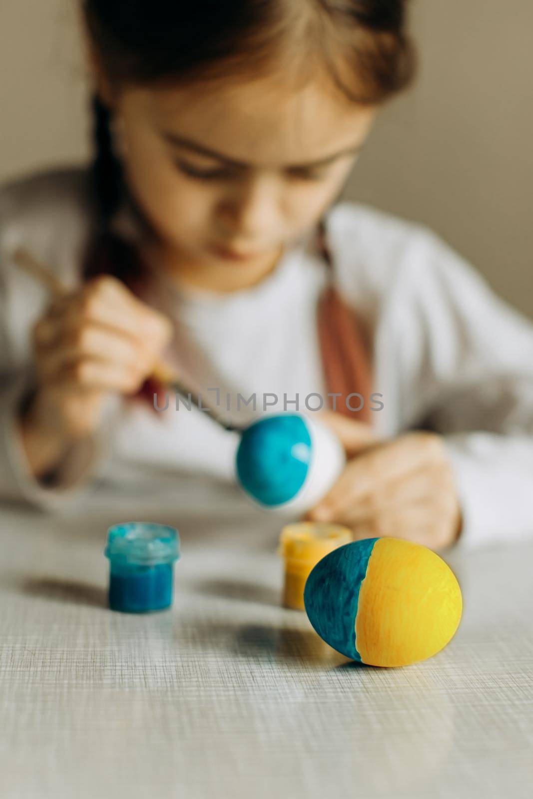 Portrait of a Ukrainian girl. the child paints the egg blue and yellow. The child loves and supports his country. Cute little child girl painting with blue and yellow colors Easter eggs. Hands of a girl with a easter egg. Close-up.