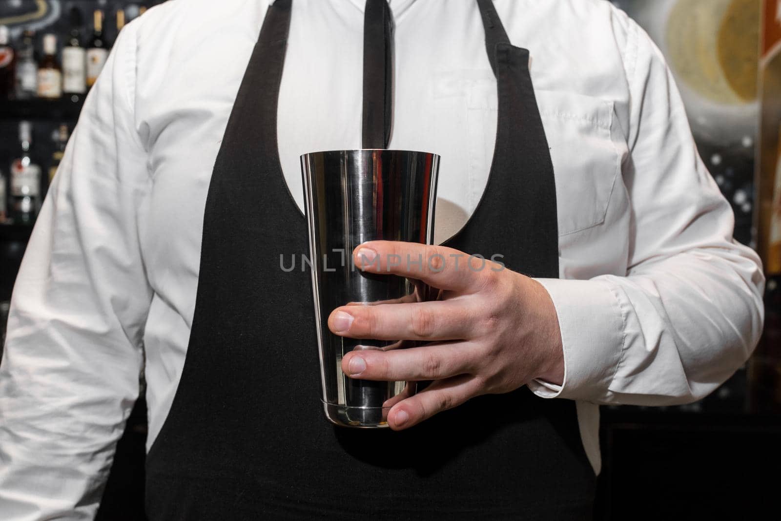 The hand of a professional bartender man holds a tool for mixing and making shaker cocktails.