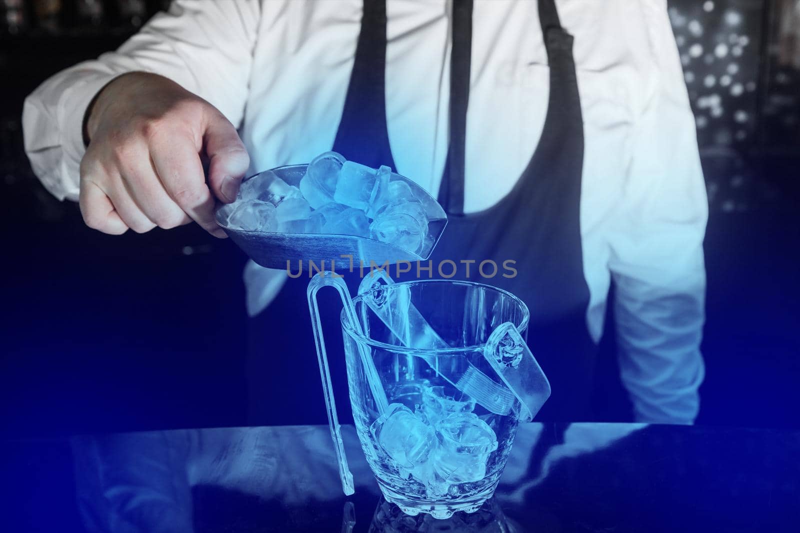 A professional bartender adds cold ice cubes on a scap to a serving dish.